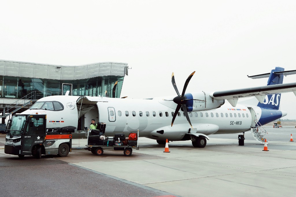 SAS turboprop on the ramp with Aviator baggage tug, loaded cart, and ground crew at the aircraft door
